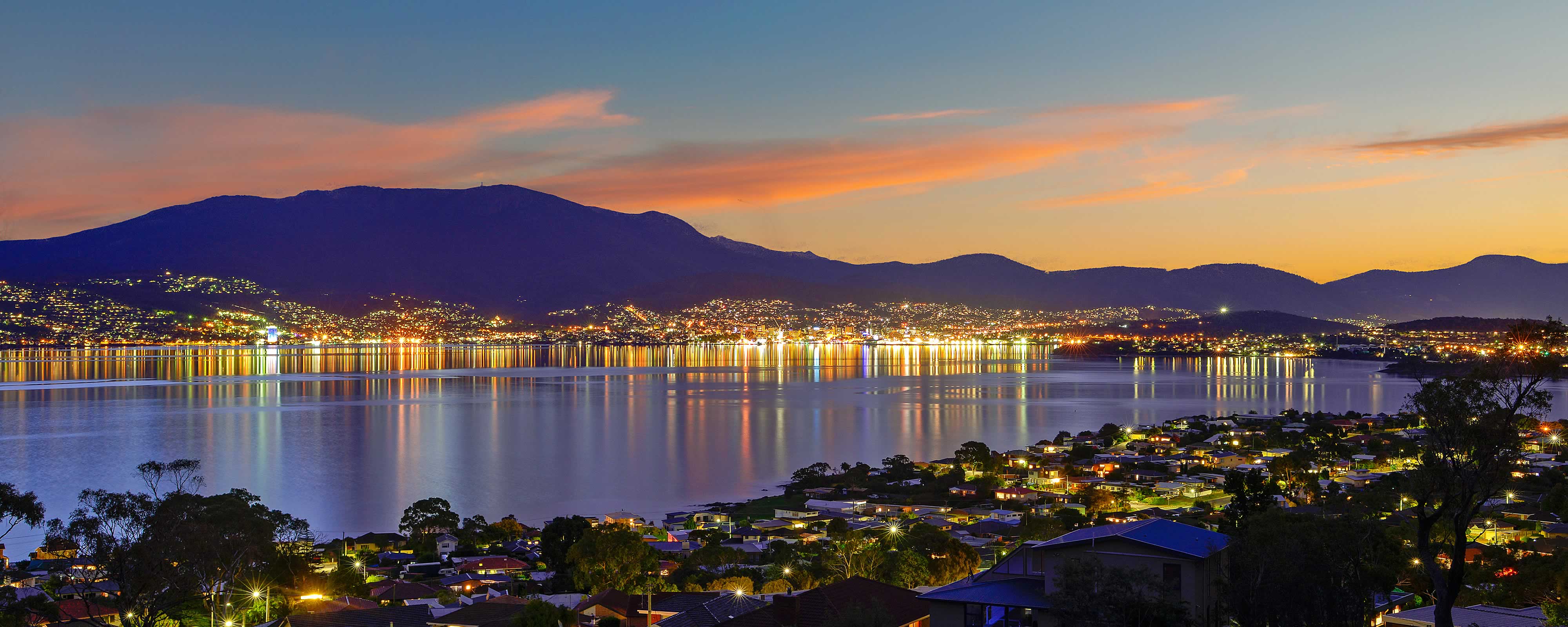 View from Tunah Street at night across the River Derwent, with the lights of Hobart and Sandy Bay reflected in the water and kunanyi / Mount Wellington in the distance. Photo: Owen Fielding.